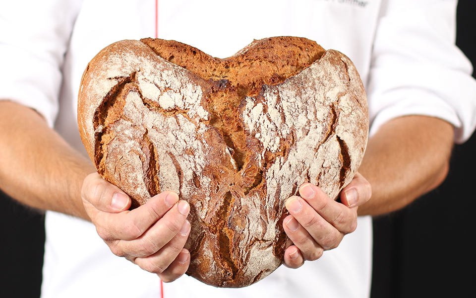 Hände halten ein herzförmiges Brot