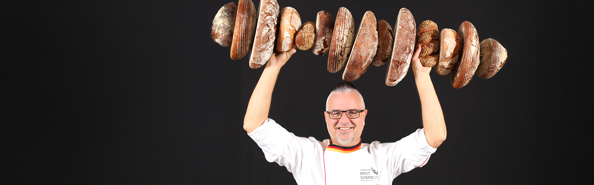Brotsommelier Harald Pommer hält eine Vielzahl an Broten über seinem Kopf