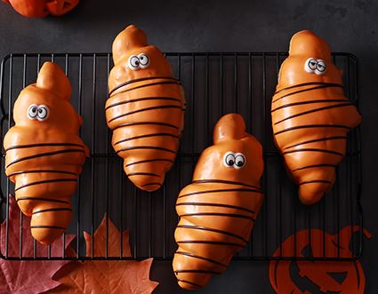 Vier orange Halloween-Geister liegen auf einem schwarzen Kuchengitter