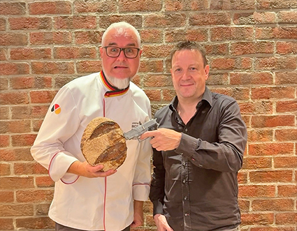 Krimiautor Josef Rauch hält eine Pistole auf ein Brot in den Händen von Brotsommelier Harald Pommer